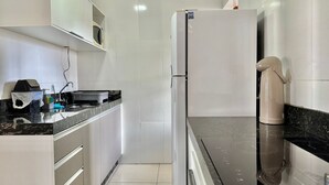 A modern kitchen with white cabinets, a black countertop, and a stainless steel refrigerator. - Residencial Falcão (Bombinhas)