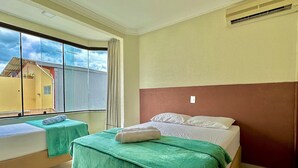 A hotel room with two beds, a large window, and a view of the outside. - Residencial Falcão (Bombinhas)