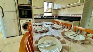 A kitchen with a dining table set for four, a washing machine, a microwave, and a refrigerator. - Residencial Falcão (Bombinhas)