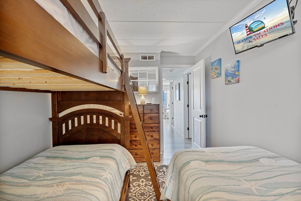 A bedroom with two beds, a wooden headboard, a TV on the wall, and a staircase leading to another room.