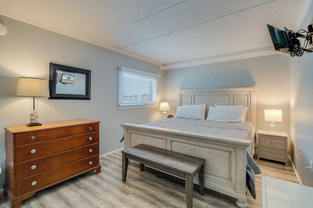 A bedroom with a bed, dresser, nightstands, and a bench.