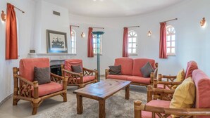 A cozy living room with wicker furniture, a fireplace, and large windows with curtains. - Villa Noras - Three Bedroom Villa, Sleeps 6 (Albufeira)