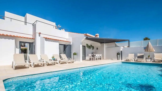 Une piscine avec des chaises longues et un espace salon abrité.