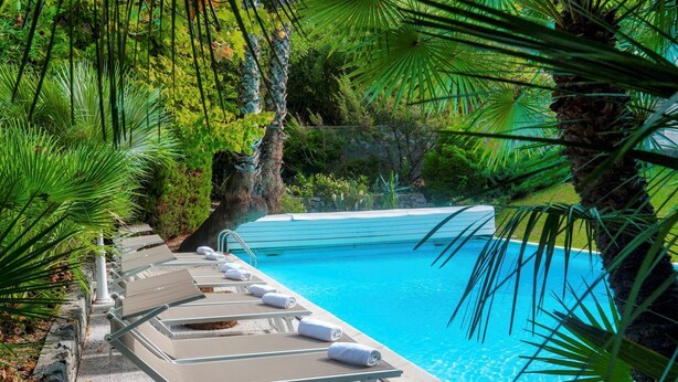 A pool area with lounge chairs and a clear blue pool surrounded by lush greenery.