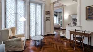 A spacious living room with a wooden herringbone floor, a round table, a sofa, and a chair.