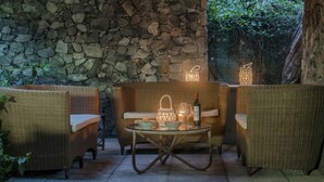 A stone wall, wicker furniture, a table with a bottle and glasses, and lanterns.