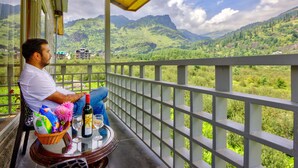 A man sitting on a balcony with a view of green hills and a clear sky. - La Aero Resort (Manali)