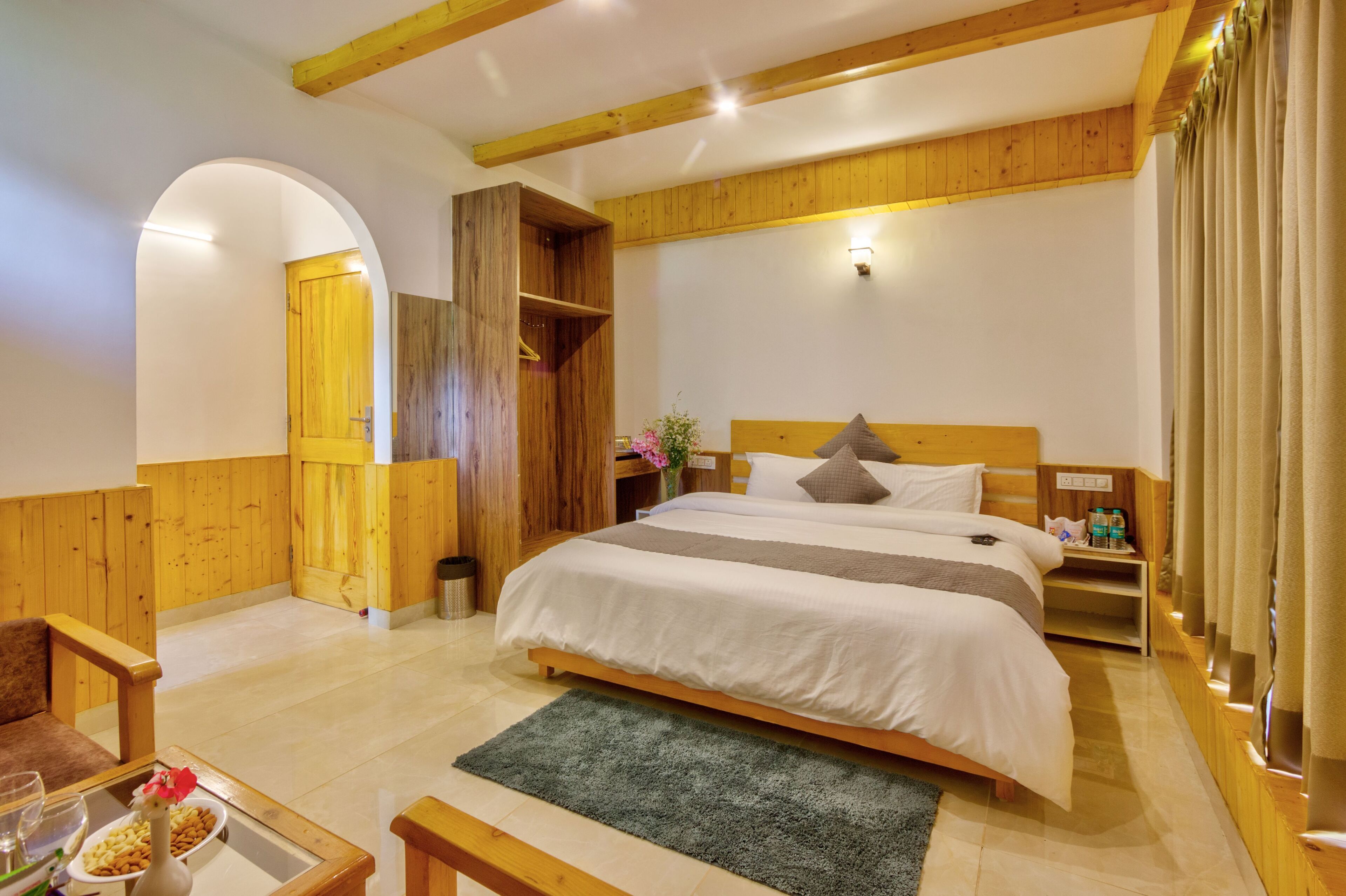 A bedroom with a large bed, wooden headboard, a small bedside table, a nightstand, a wooden wardrobe, a mirror, and a green rug.