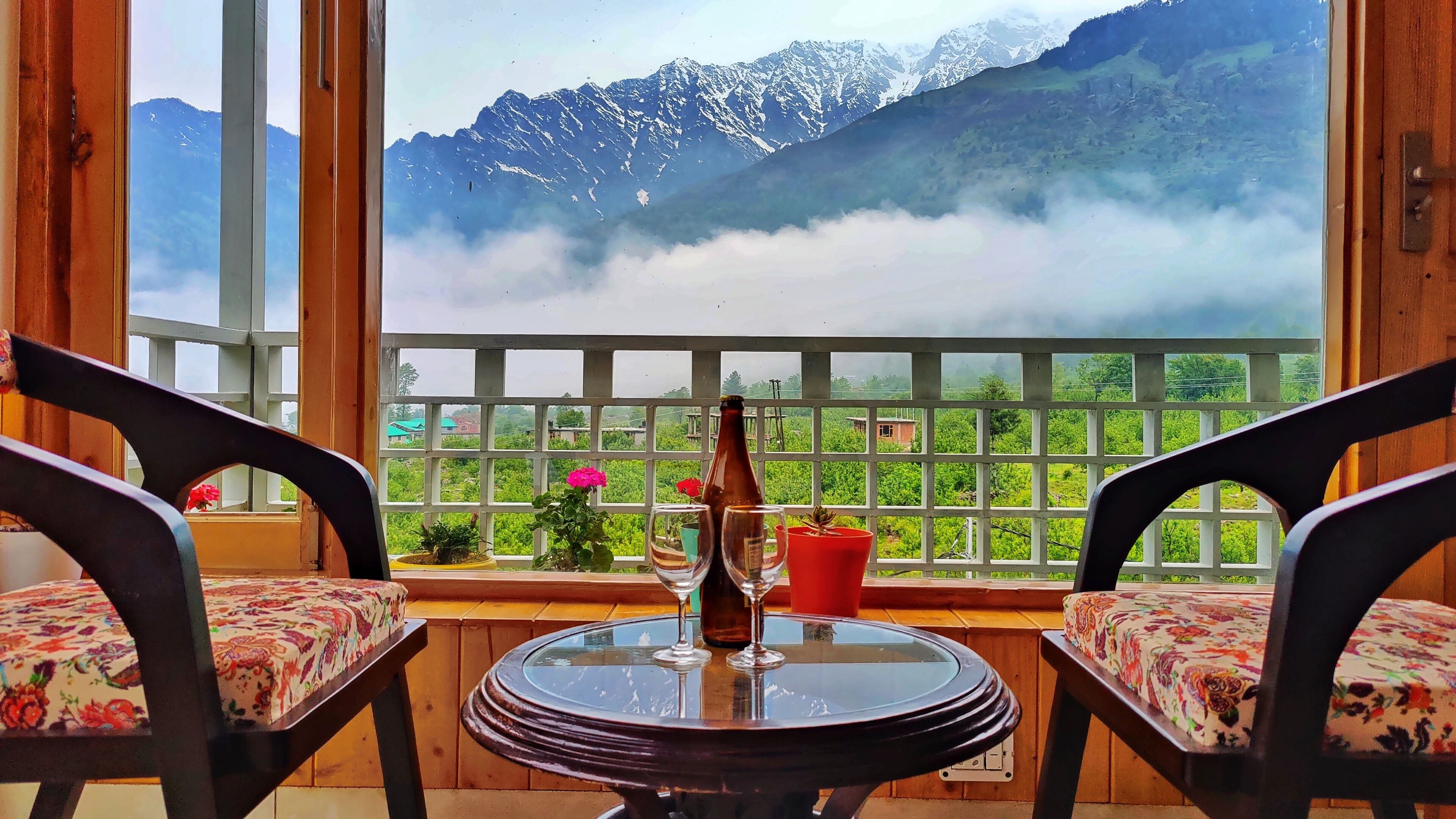 A balcony with two chairs, a table, and a bottle of wine.