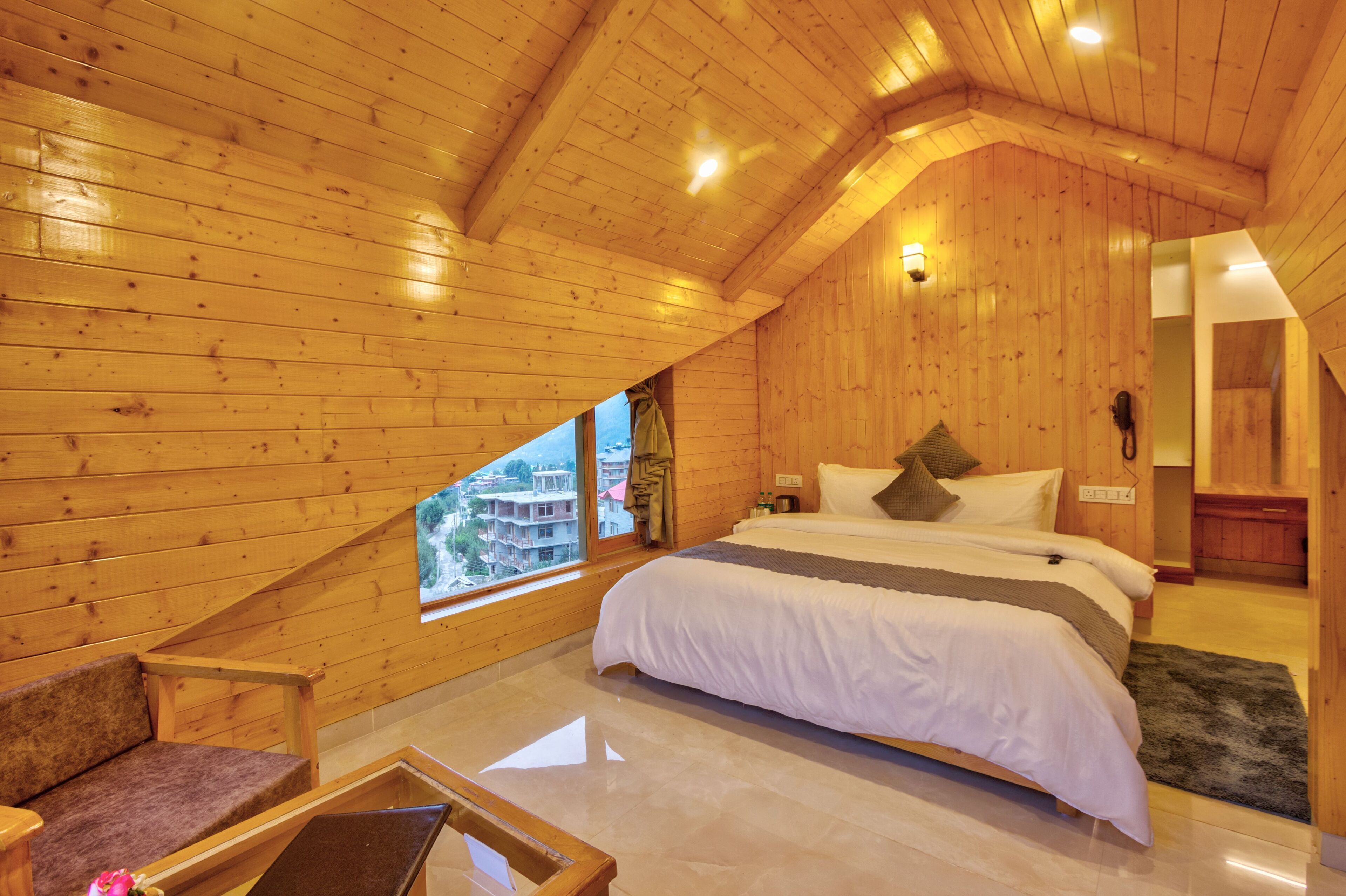 A wooden-paneled bedroom with a bed, a sofa, a window with a view, and a small bathroom area.