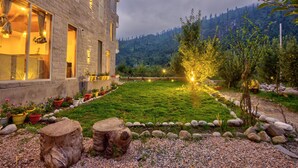A stone building with large windows, a well-maintained garden with a variety of potted plants, and a view of a forested mountain range. - La Aero Resort (Manali)