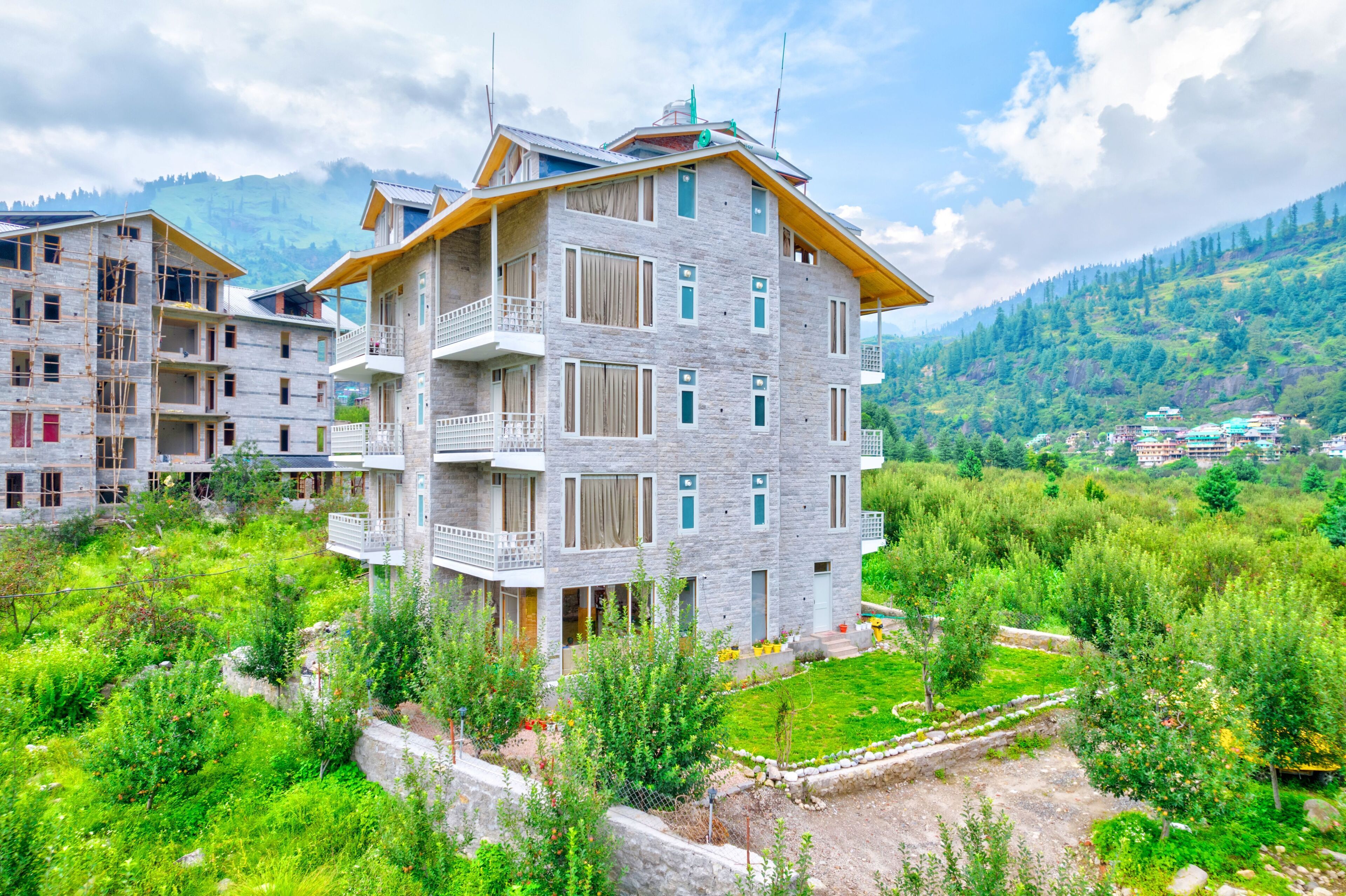 A multi-story building with balconies, surrounded by lush greenery and mountains in the background.