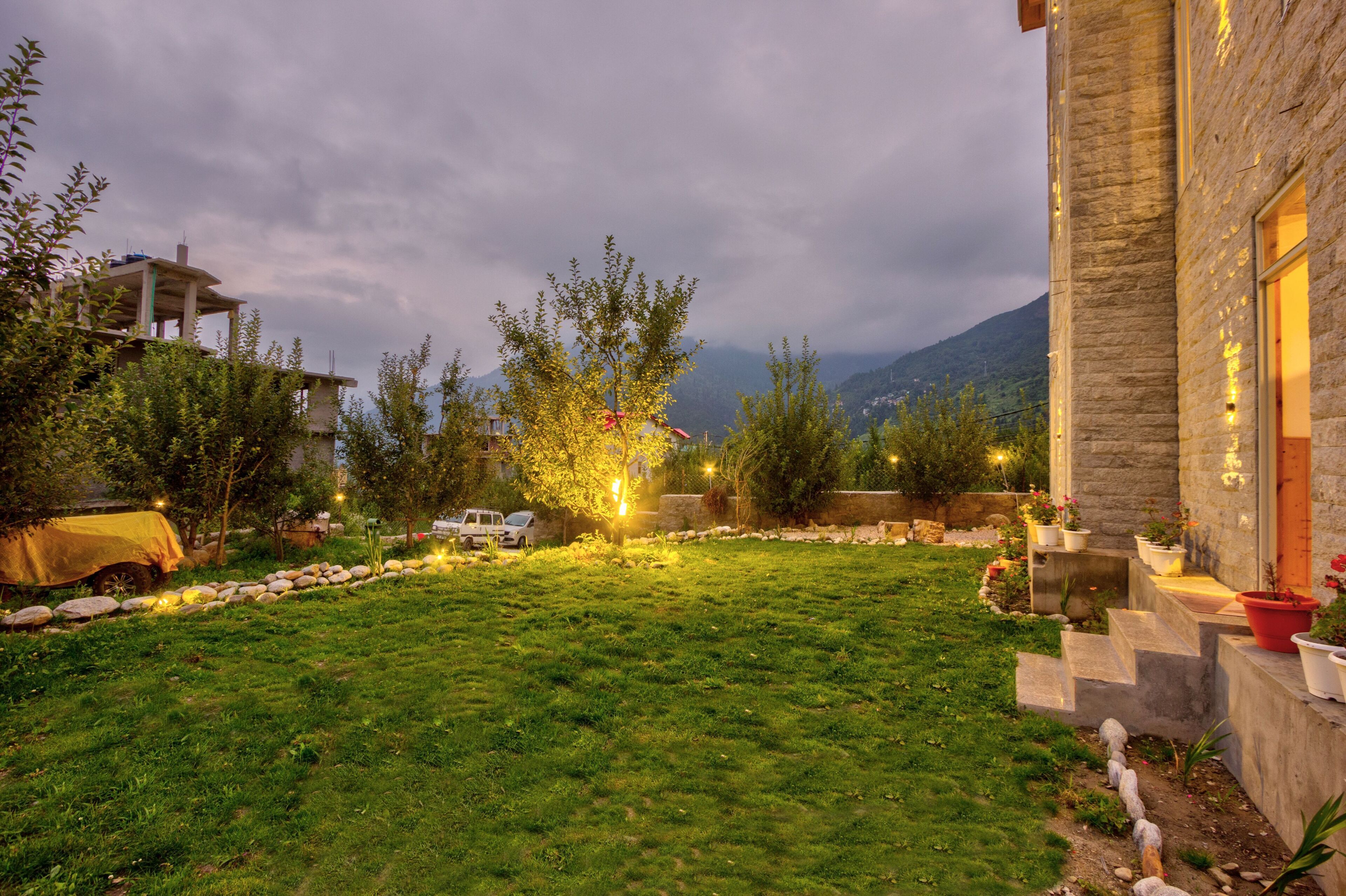 Un edificio in pietra con un prato curato, illuminazione esterna e vista sulle montagne sullo sfondo.