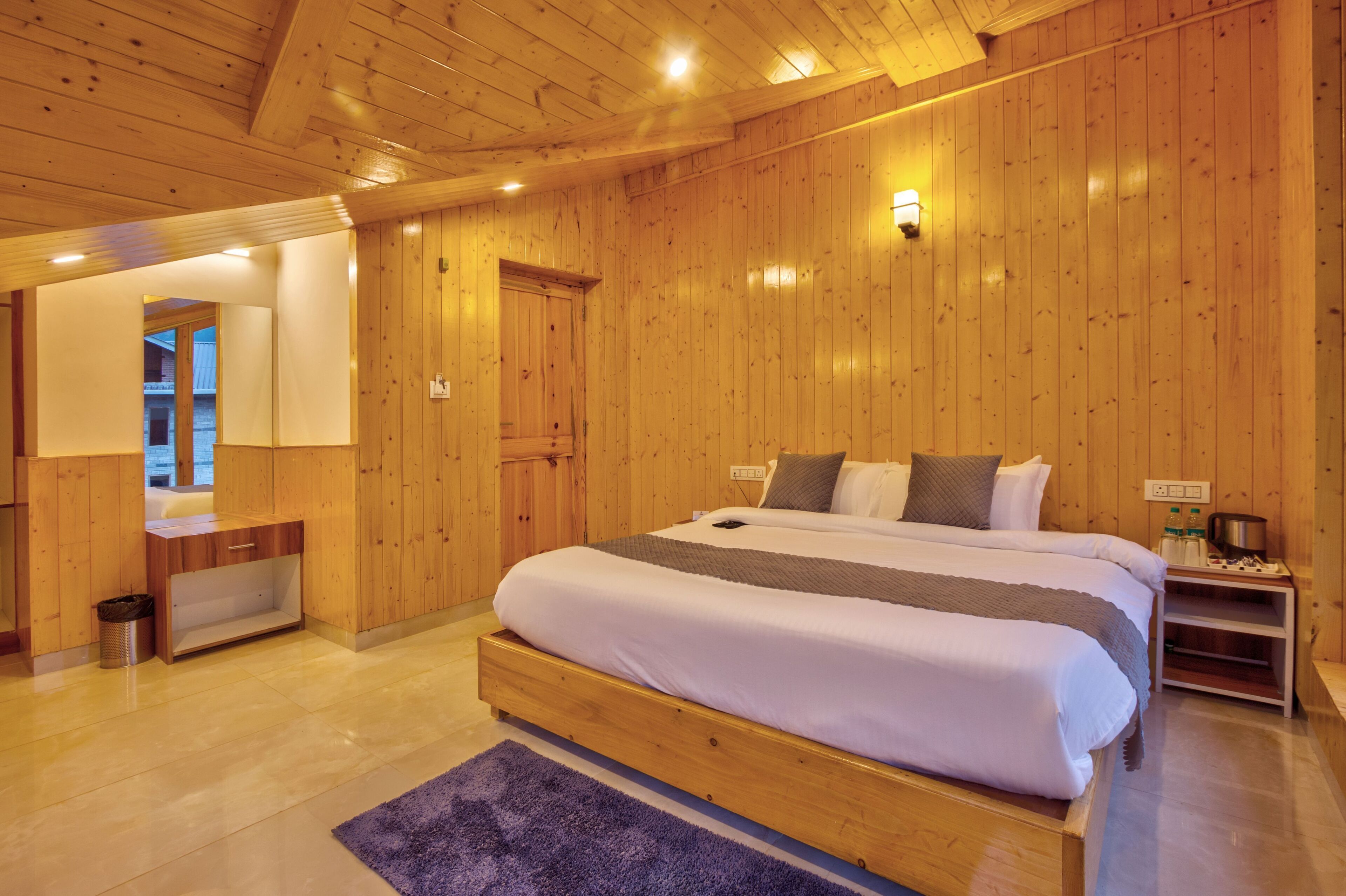 A wooden-paneled bedroom with a large bed, a nightstand, and a mirror.