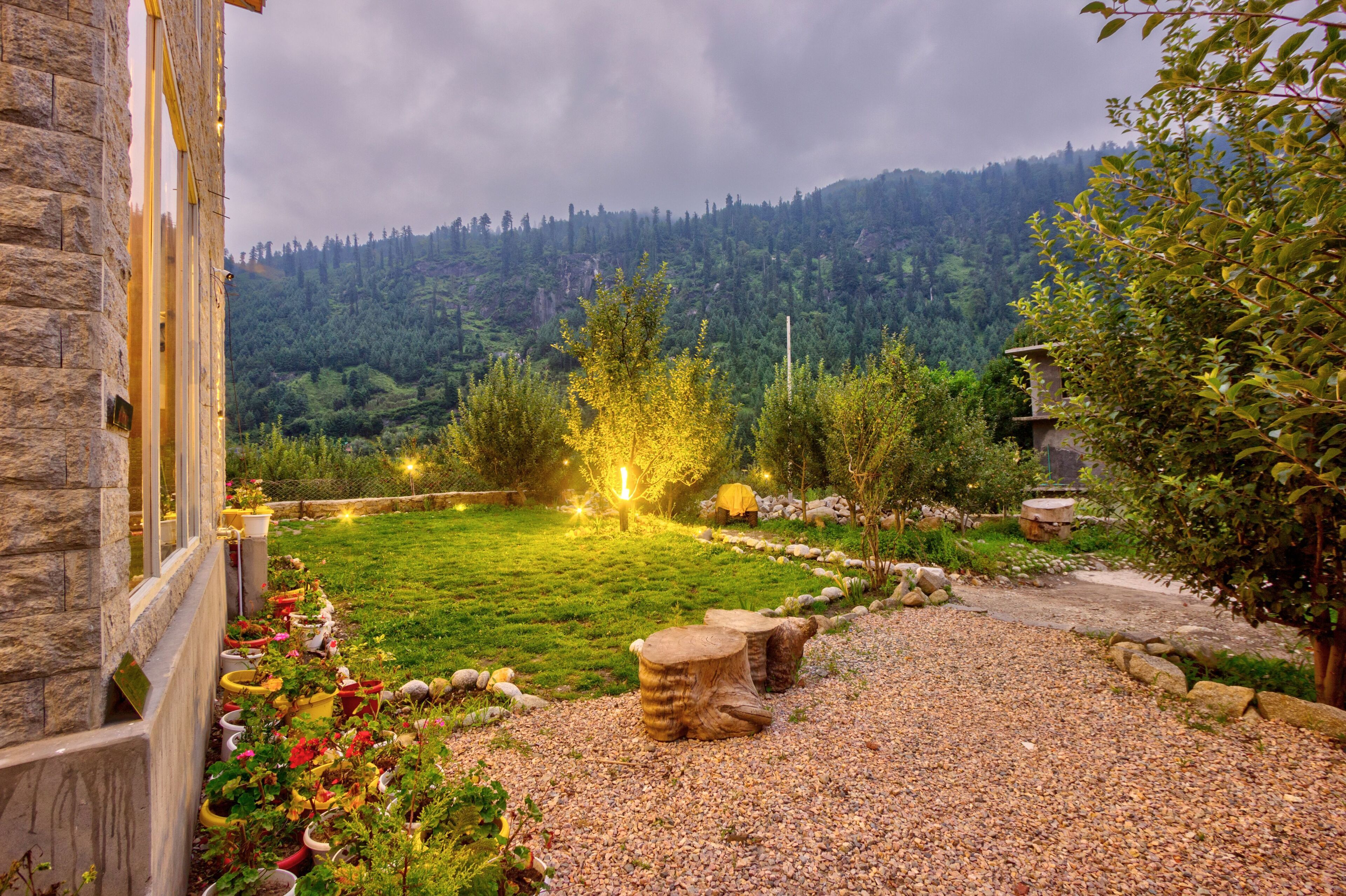 A stone building with a garden featuring a gravel path, wooden stools, and potted plants.