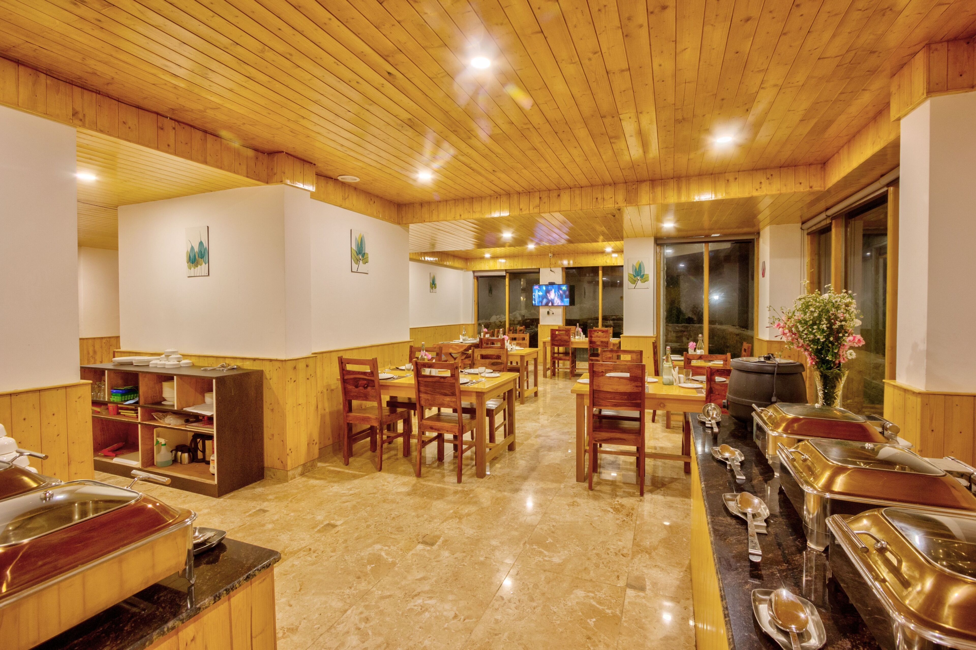 A restaurant with wooden tables and chairs, buffet counters, and a television screen.