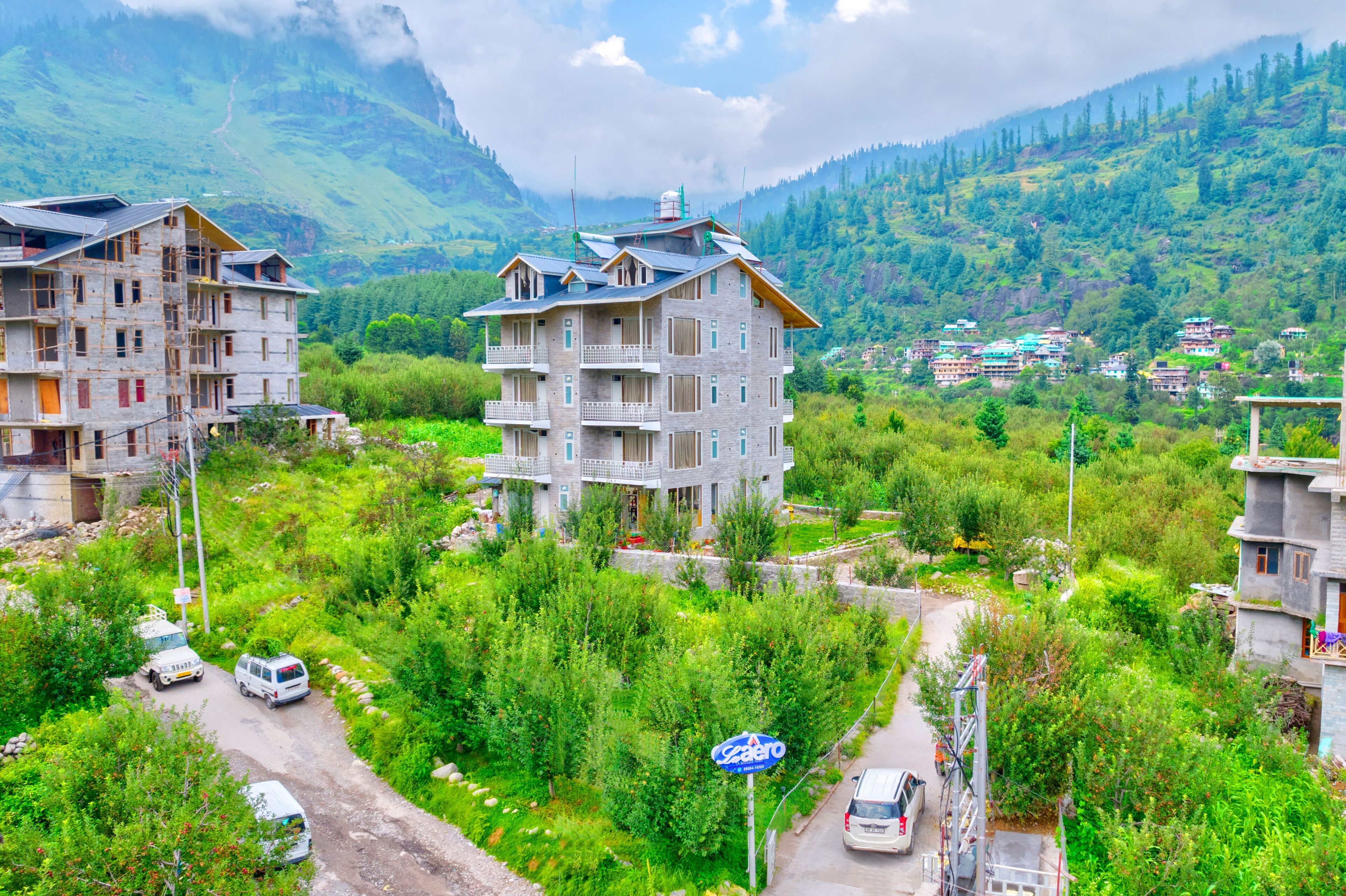 A multi-story building with balconies, surrounded by lush greenery and mountains in the background.