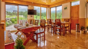 A wooden interior with a dining area, large windows, and a TV. - La Aero Resort (Manali)