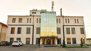 A hotel with a modern glass facade, a prominent 'M' logo, and a parking lot with cars. - Macao Hotel (Yerevan)