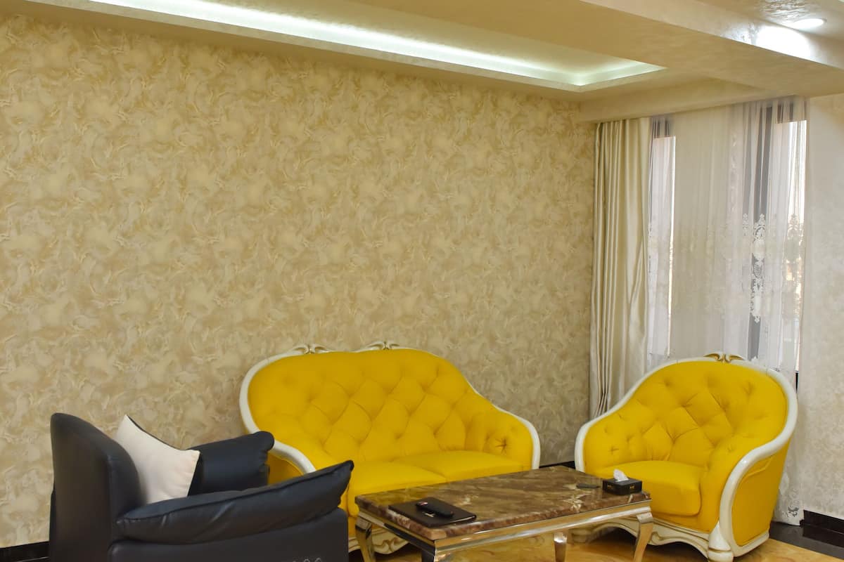 Ein Zimmer mit Marmorboden, zwei gelbe Sessel, ein dunkles Sofa und einem Holztisch.