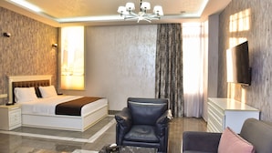 A modern hotel room with a large bed, a leather armchair, a sofa, a flat-screen TV, and a chandelier. - Macao Hotel (Yerevan)