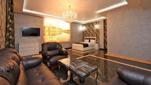A modern living room with leather sofas, a glass coffee table, a TV mounted on the wall, and a chandelier. - Macao Hotel (Yerevan)