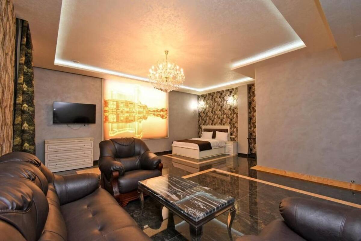 Ein modernes Wohnzimmer mit Ledersofas, einem Glastisch, einem an der Wand montierten Fernseher und einer Chandelieber.