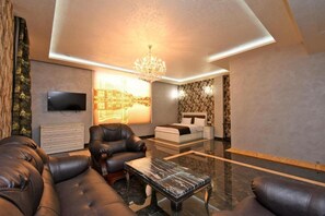 A modern living room with leather sofas, a glass coffee table, a TV mounted on the wall, and a chandelier. - Macao Hotel (Yerevan)