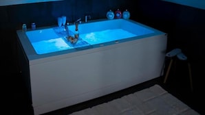 A modern bathroom with a large bathtub, a handheld showerhead, and three bottles of soap. - Yacht Club Angioino (Naples)