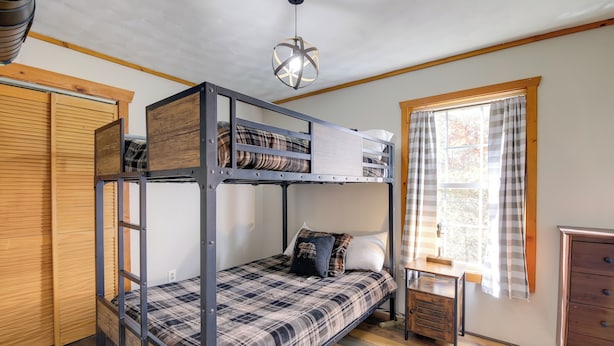 Habitación con literas, un armario de madera, una mesita y una ventana con cortinas.
