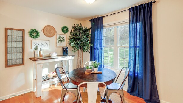 A dining area with a round wooden table, four chairs, a white console table with a plant, and a window with blue curtains. - Virginia Escape w/ Patio & Fire Pit, Near Hiking! (Speedwell)