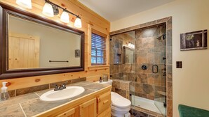 Un baño con tocador de madera, un espejo grande, un lavabo, un inodoro y una zona de ducha con cerramiento de vidrio.