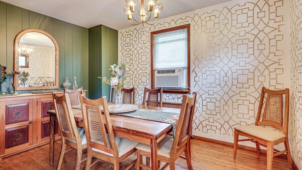 Une salle à manger avec une table en bois, des chaises, un lustre et un papier peint à motifs.