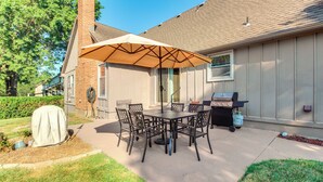 Een terras buiten met een tafel, stoelen, een barbecue en een overdekte parasol.
