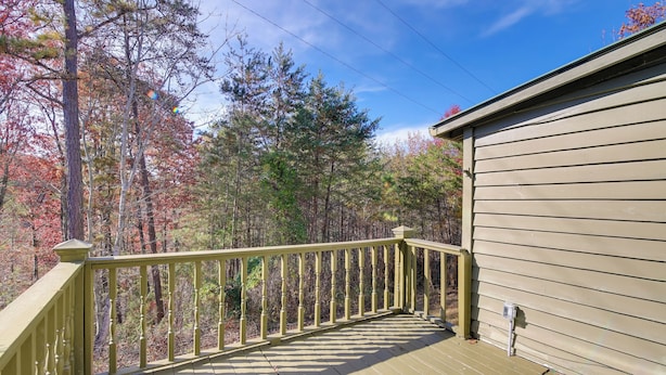 A wooden deck with a railing, surrounded by trees with autumn foliage. - 'faith Cabin' in Cosby: Fire Pit + Covered Deck (Cosby)