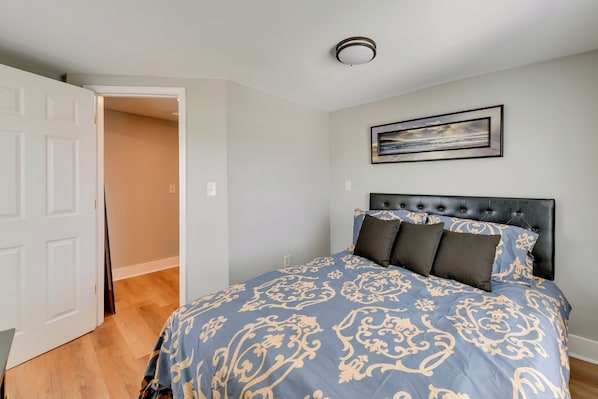 Quarto com cama, cabeceira, quadro na parede e porta que dá para outro cômodo.
