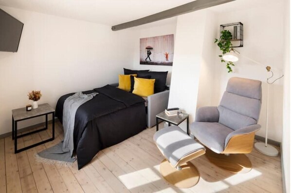 Een moderne slaapkamer met een bed, nachtkastje, stoel en een schilderij aan de muur.
