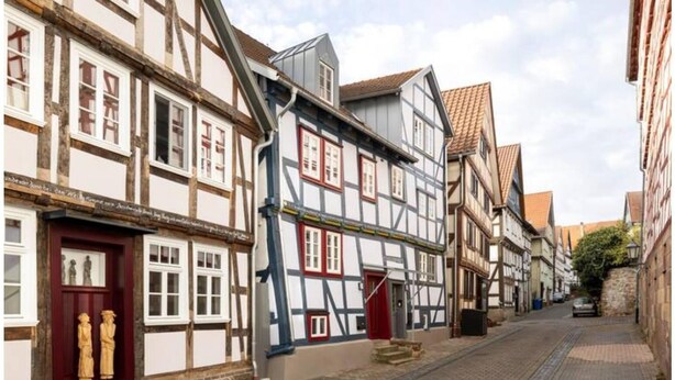 Una estrecha calle adoquinada flanqueada por edificios tradicionales con entramado de madera, cada uno con una fachada diferente, vigas de madera a la vista y enlucido blanco.