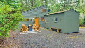 A cabin with a gravel driveway, wooden chairs, a fire pit, and a small shed.