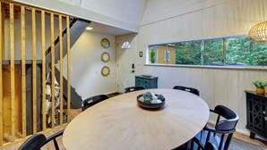 A modern dining area with a round table, chairs, and a decorative bowl. A staircase with wooden railings is visible on the left.