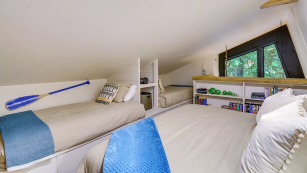 Une chambre de dortoir avec des lits superposés, une bibliothèque et une fenêtre donnant sur les arbres.