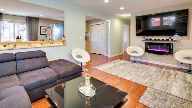 A modern living room with a sectional sofa, two white chairs, a flat-screen TV, and a fireplace. - Serene Springfield Retreat on 6 Acres w/ Hot Tub! (Springfield)
