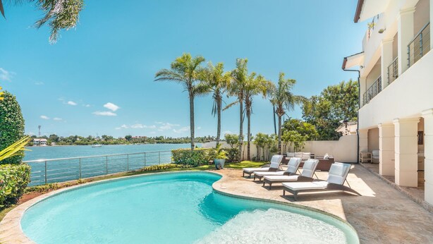 Una piscina con sillones de descanso, vista al mar y palmeras.