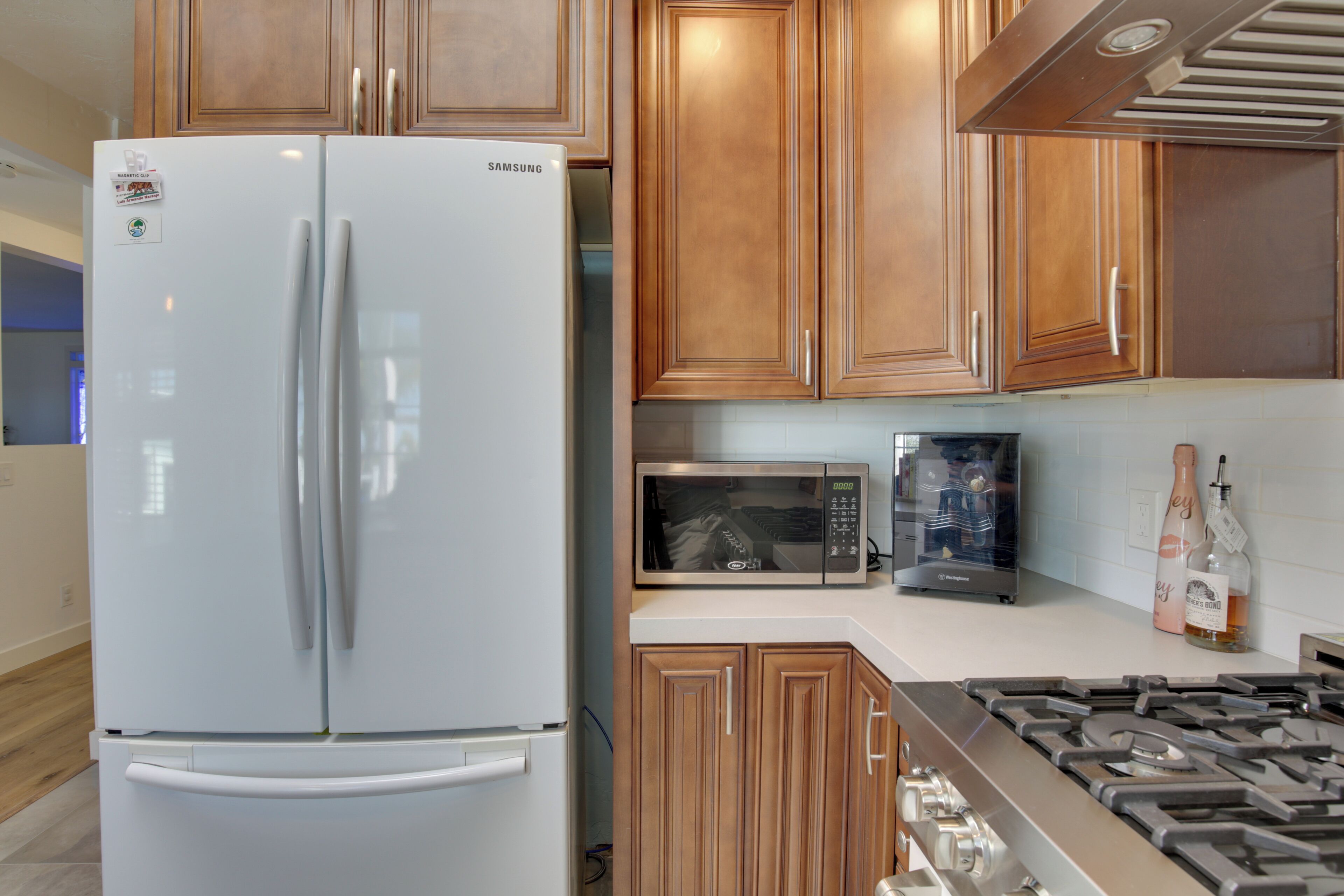 Une cuisine avec un réfrigérateur blanc, un four à micro-ondes en acier inoxydable, des armoires en bois et une cuisinière à gaz.