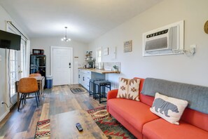 A modern living room with a sofa, a coffee table, and a TV. There is a kitchen area with a fridge, microwave, and cabinets. - Cozy Hope Cabin Vacation Rental in Cosby w/ View (Cosby)