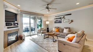 A modern living room with a fireplace, a ceiling fan, a sofa set, and a dining area with a view. - Boat Slip + Pool Access: Osage Beach Retreat (Osage Beach)