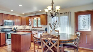 Una cocina con armarios de madera, una isla central, una mesa de comedor con sillas y una araña.
