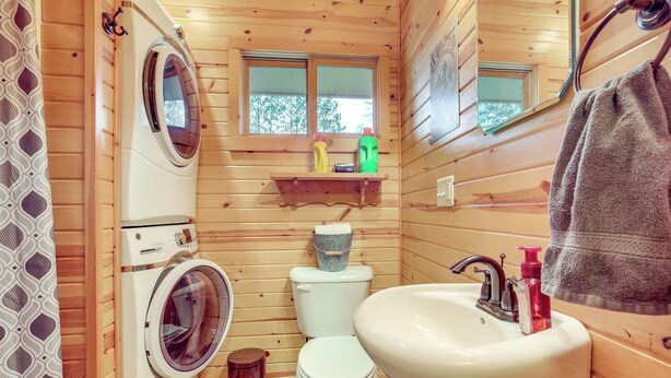 Un baño pequeño y acogedor de madera con lavadora, inodoro, lavabo y un ventanal.