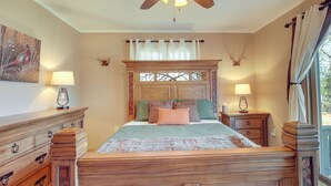 Un dormitorio con cama de madera, dos mesitas de noche con lámparas, un ventilador de techo y una ventana con cortinas.
