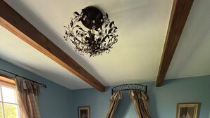 A bedroom with a four-poster bed, a chandelier, and a view of the outdoors through a window.